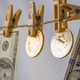 Clothes pins on a string hold up 100 dollar bills alongside crypto coins with the bitcoin symbol.